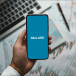 Eine Hand hält ein Smartphone mit dem Logo von Ballard Power Systems auf dem Display vor einem Hintergrund mit Finanzdiagrammen und einem Laptop.