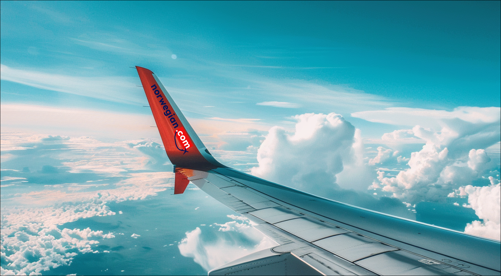 die Flügelspitze eines Flugzeugs mit dem Schriftzug norwegian.com und einem markanten roten Endteil, das gegen einen klaren Himmel und weiße Wolken abgehoben ist.