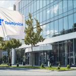 eine wehende Flagge mit dem Logo von Telefónica vor einem modernen Bürogebäude an einem sonnigen Tag.