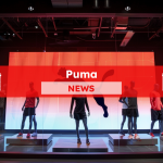 eine Sportbekleidungs-Auslage mit mehreren Schaufensterpuppen, die vor einem großen Puma-Logo aufgestellt sind, mit einem Puma NEWS Banner