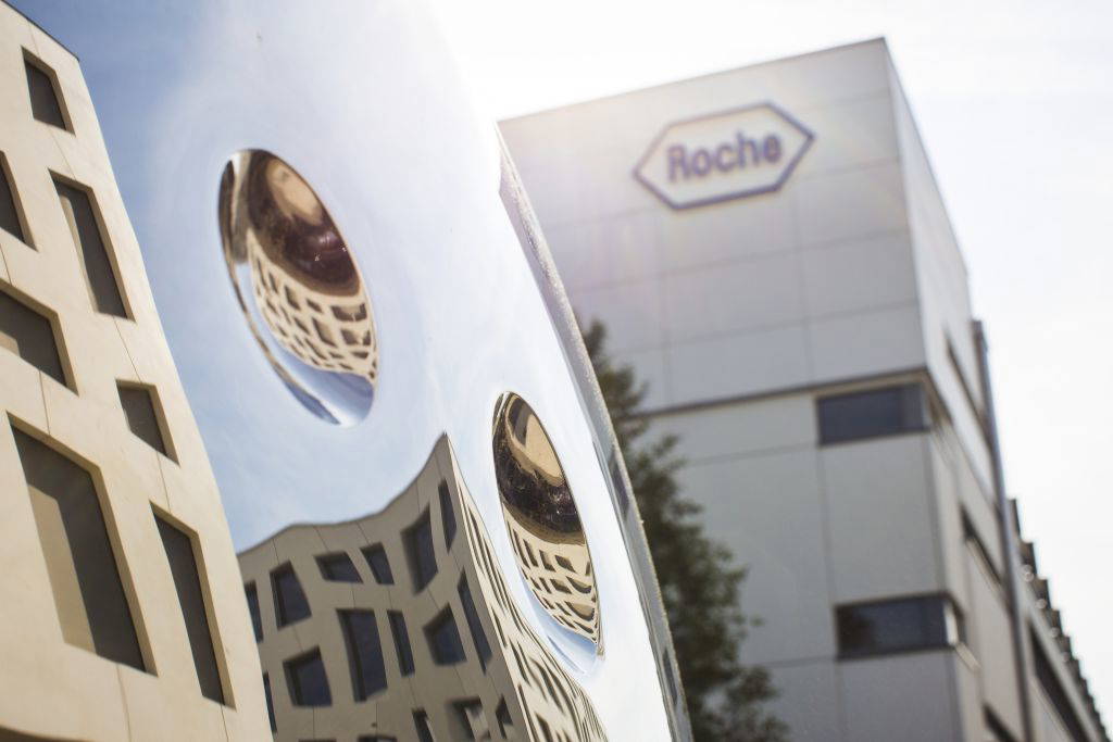 Spiegelung moderner Architektur in einer glänzenden Skulptur, im Hintergrund das Roche-Logo auf einem Firmengebäude.
