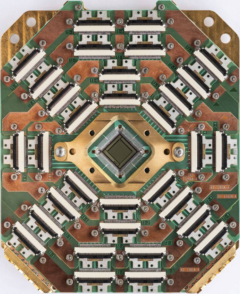 Nahaufnahme eines komplexen Quantenchips von D-Wave mit zahlreichen Steckverbindungen und einem zentralen Prozessor.