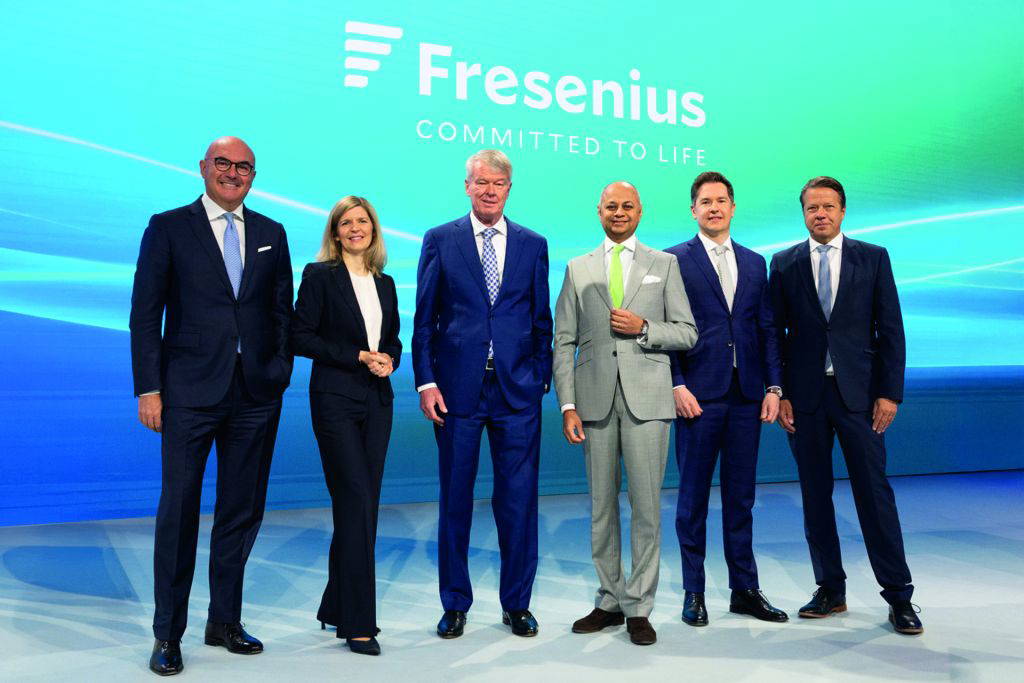 Das Führungsteam von Fresenius steht in Businesskleidung auf einer Bühne vor einem großen Bildschirm mit dem Firmenlogo und dem Slogan „Committed to Life“.