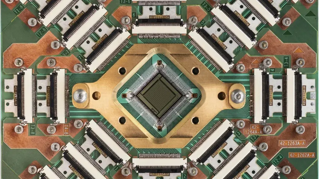 Nahaufnahme eines komplexen Quantenchips von D-Wave mit zahlreichen Steckverbindungen und einem zentralen Prozessor.