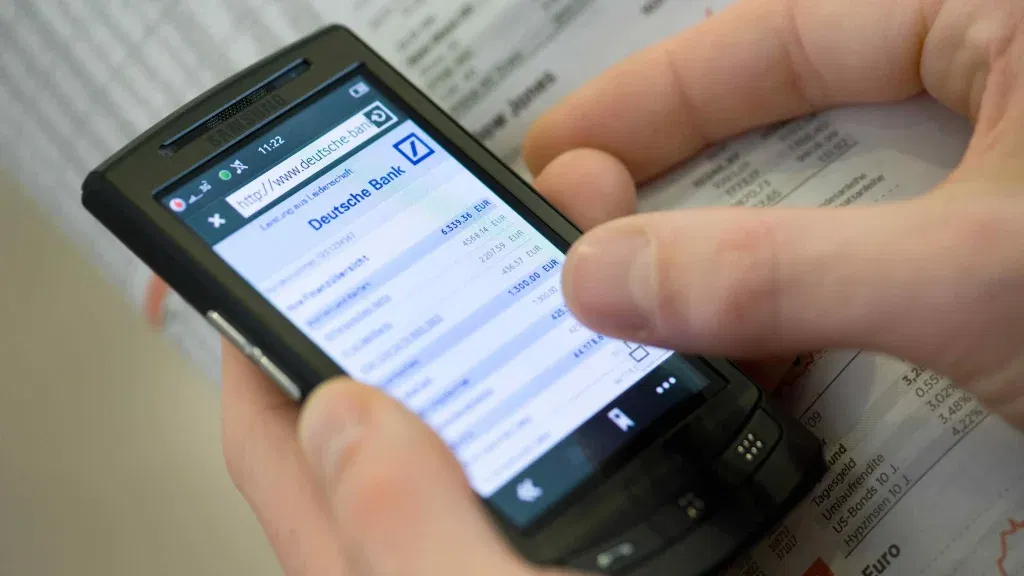 Hände bedienen ein Smartphone mit geöffneter Deutsche-Bank-App – Onlinebanking unterwegs auf dem Prüfstand.