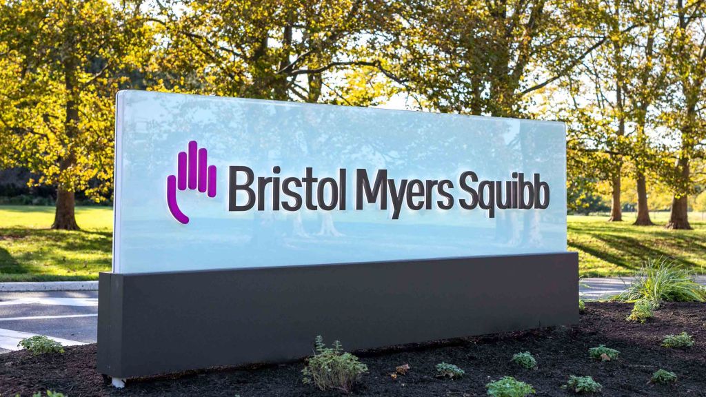 Firmenschild von Bristol Myers Squibb vor dem Unternehmensgelände, mit Logo und Schriftzug, im Hintergrund Bäume und Grünfläche. © Bristol-Myers Squibb