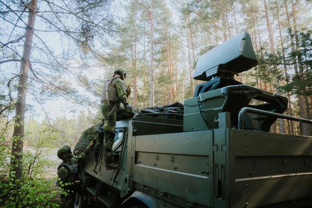 Militärfahrzeug im Wald mit montiertem Saab-Giraffe-1X-Radarsystem, bedient von zwei Soldaten in Tarnuniform; das Radar ist auf dem Fahrzeugdach installiert und für den mobilen Einsatz ausgelegt.