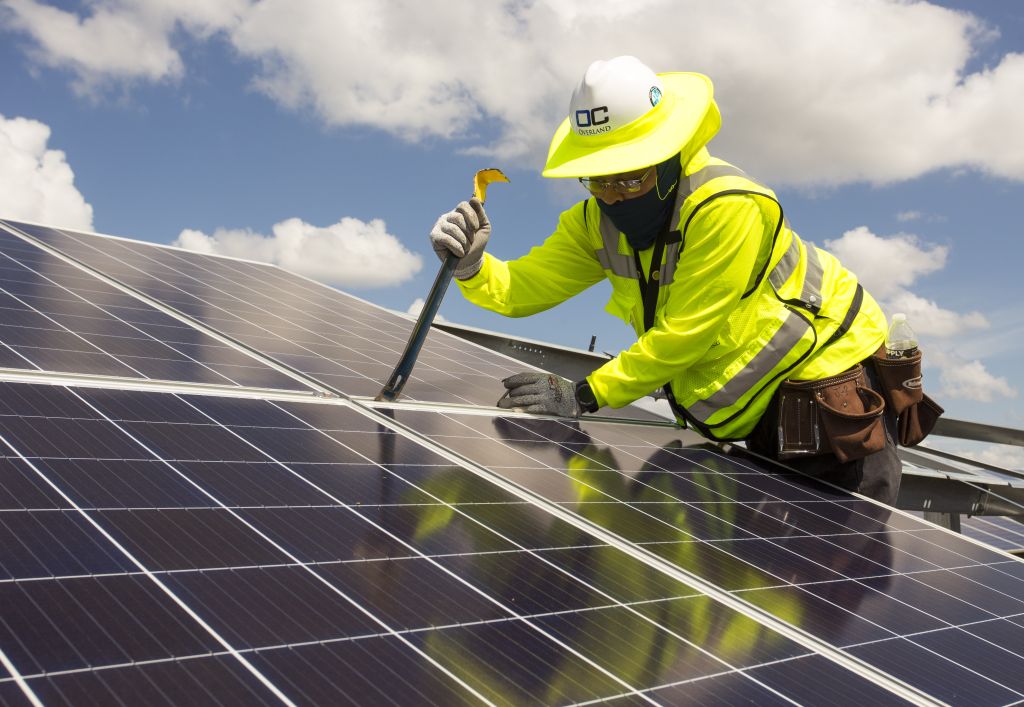 NextEra Energy: Mit Google in die neue Strom-Ära! Ein Techniker in gelber Sicherheitskleidung installiert oder wartet Solarmodule unter blauem Himmel. Das Bild symbolisiert den Ausbau erneuerbarer Energien und nachhaltige Energieinfrastruktur.