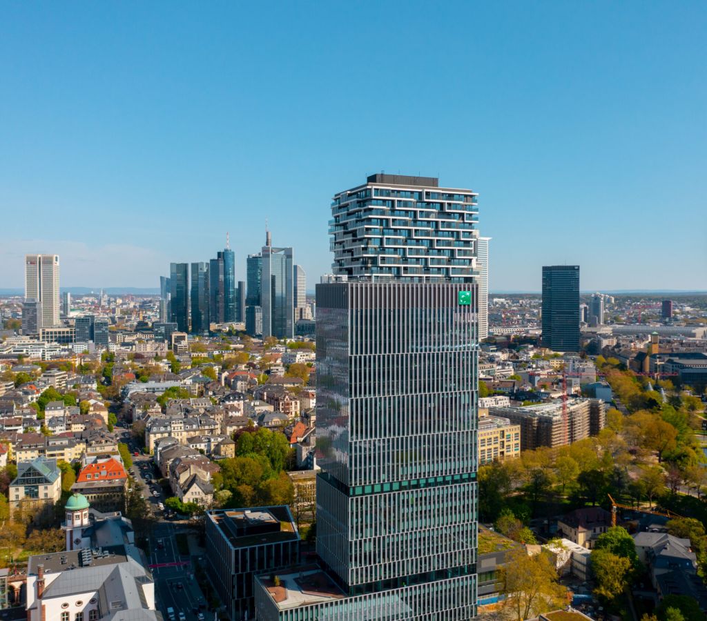 BNP Paribas-Aktie: Das läuft jetzt! Der Senckenberg-Turm in Frankfurt mit dem grünen BNP-Paribas-Logo im Vordergrund, dahinter die Frankfurter Skyline mit mehreren Hochhäusern an einem klaren, sonnigen Tag.