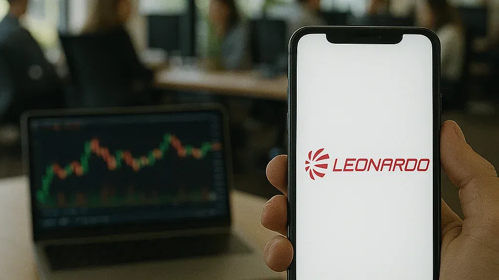 Leonardo-Aktie: Milliarden-Auftrag aus Großbritannien sichert Standort! In einem modernen, lichtdurchfluteten Großraumbüro hält eine Hand ein Smartphone mit dem rot leuchtenden Leonardo-Logo auf dem Bildschirm. Im Hintergrund arbeitet eine Gruppe von Menschen an Schreibtischen, während auf einem Laptop ein Aktienchart angezeigt wird.
