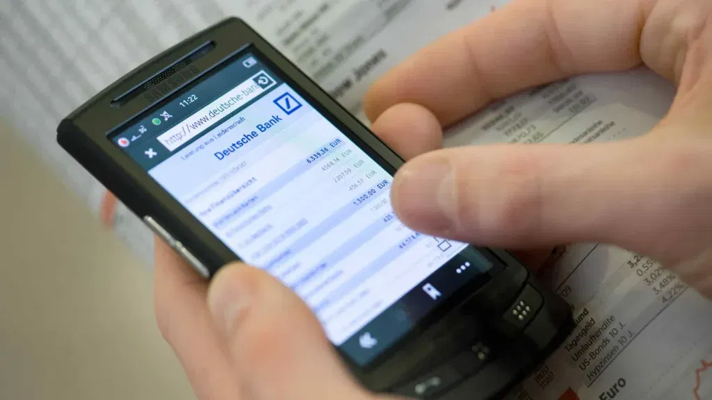 Deutsche Bank-Aktie: startet neuen Anlauf – Bewertung günstig, Trend stabil! Hände bedienen ein Smartphone mit geöffneter Deutsche-Bank-App – Onlinebanking unterwegs auf dem Prüfstand.