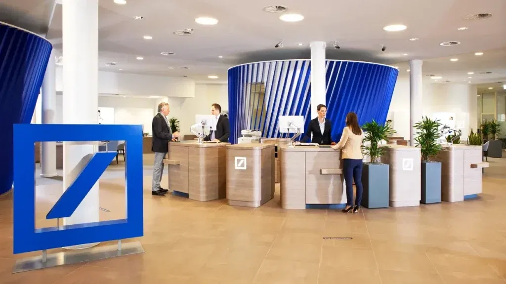 Deutsche Bank-Aktie: Jetzt wird es richtig spannend! Innenansicht einer modernen Deutsche-Bank-Filiale mit Kundenberatung an offenen Schaltern – Fokus auf persönlichen Service.