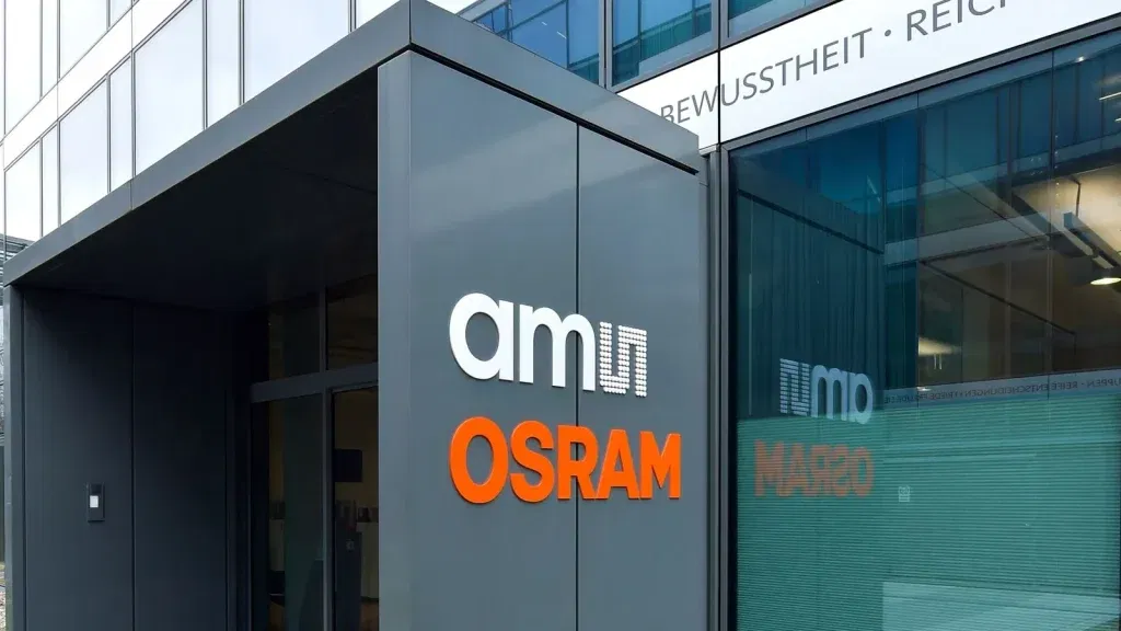 Eingangsbereich eines modernen Bürogebäudes mit Glasfassade, an dem groß das Logo „ams OSRAM“ angebracht ist. Die Spiegelung im Fenster zeigt den Schriftzug erneut. Die Szene wirkt professionell und aufgeräumt.